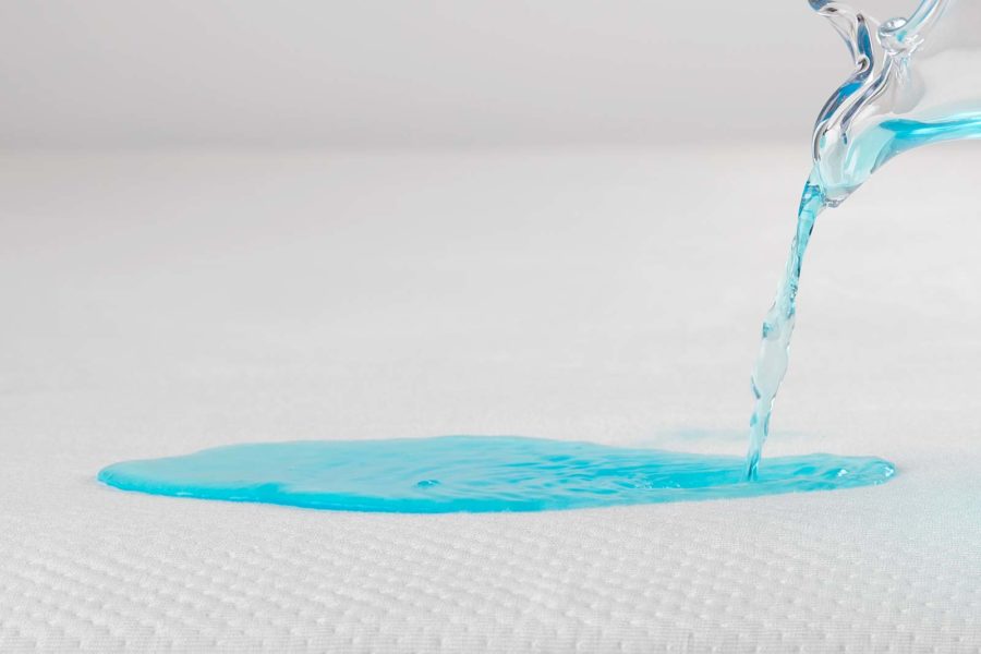 Blue liquid being poured on white mattress protector.